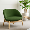Green armchair with wooden legs in a room with a plant and table.